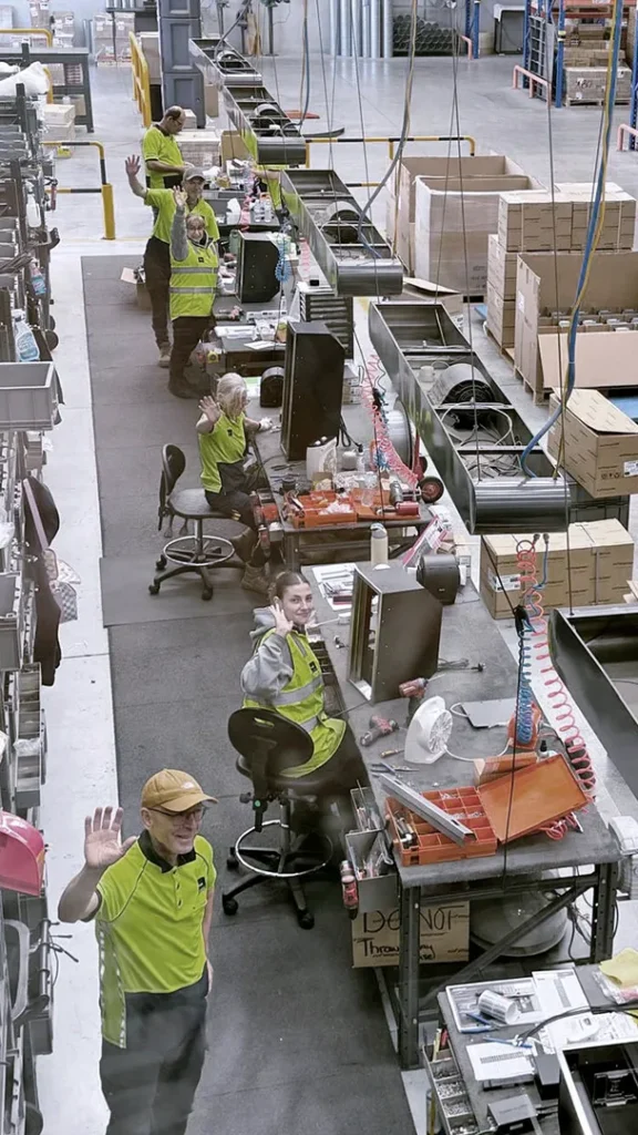Top down view of the factory floor with staffs waving from their assembly stations